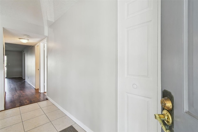 hall featuring light tile patterned floors, a textured ceiling, and baseboards