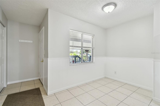 empty room with a wainscoted wall, a textured ceiling, and light tile patterned floors