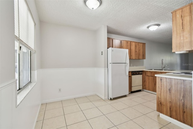 kitchen featuring white appliances, brown cabinetry, light countertops, a sink, and light tile patterned flooring