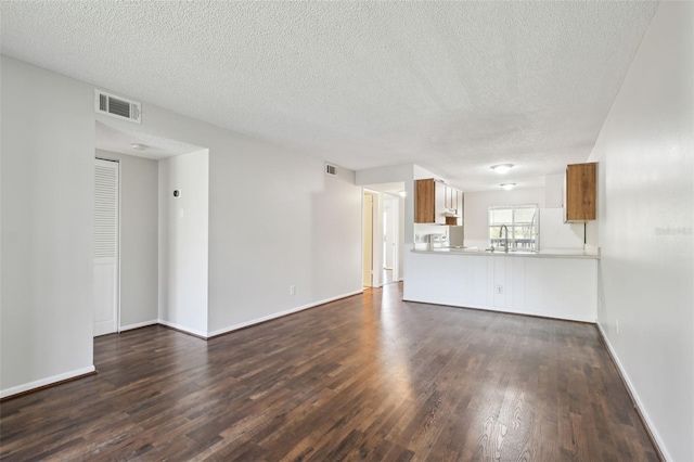 unfurnished living room with dark wood-style floors, visible vents, a sink, and baseboards