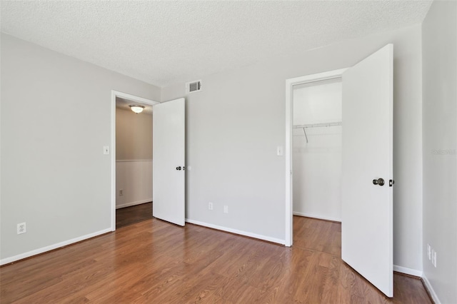 unfurnished bedroom featuring a spacious closet, a textured ceiling, visible vents, and wood finished floors