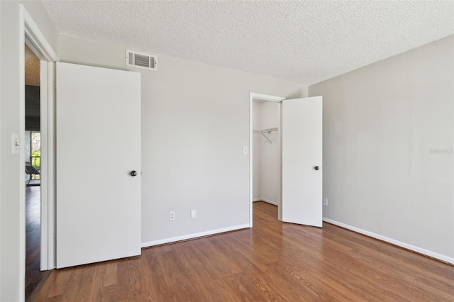 unfurnished bedroom featuring baseboards, a textured ceiling, visible vents, and wood finished floors