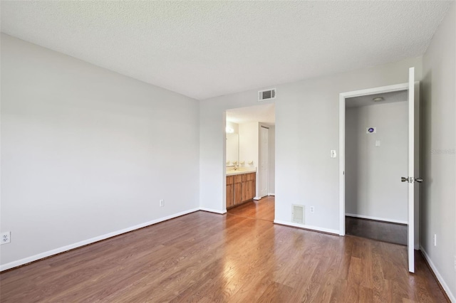 unfurnished bedroom with visible vents, a textured ceiling, baseboards, and wood finished floors