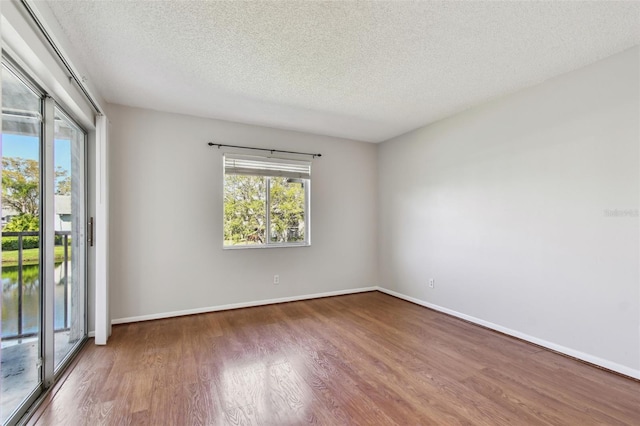 unfurnished room with a textured ceiling, wood finished floors, and baseboards