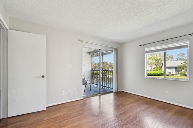 unfurnished room with a textured ceiling, baseboards, and wood finished floors