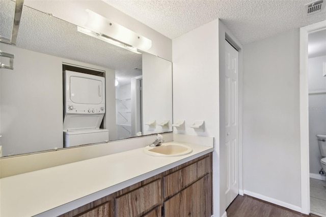 bathroom featuring a textured ceiling, toilet, visible vents, vanity, and stacked washing maching and dryer