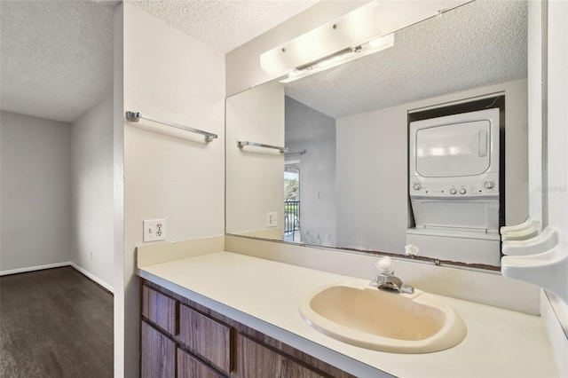 bathroom with baseboards, wood finished floors, a textured ceiling, vanity, and stacked washing maching and dryer