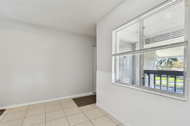 tiled spare room featuring a textured ceiling and baseboards