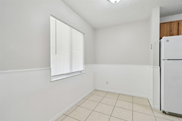 unfurnished dining area featuring a wainscoted wall, plenty of natural light, a textured ceiling, and light tile patterned floors