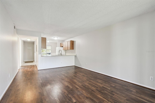 unfurnished living room featuring a textured ceiling, dark wood finished floors, visible vents, and baseboards