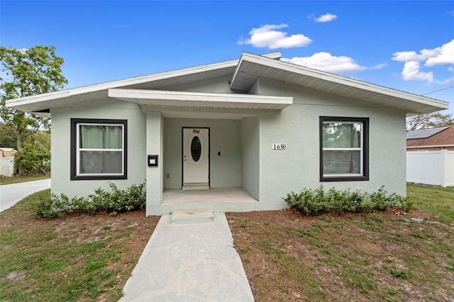 bungalow-style house with covered porch, a front lawn, and stucco siding