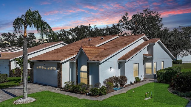 view of front of house with an attached garage, a tile roof, a lawn, and decorative driveway