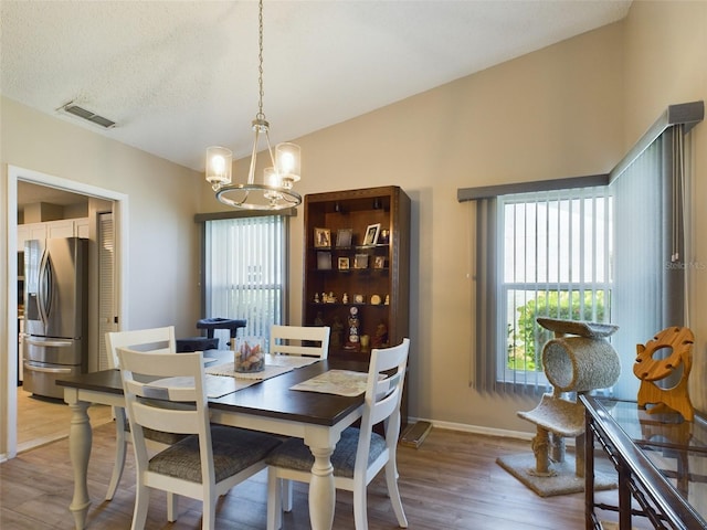 dining space with a notable chandelier, wood finished floors, visible vents, baseboards, and vaulted ceiling