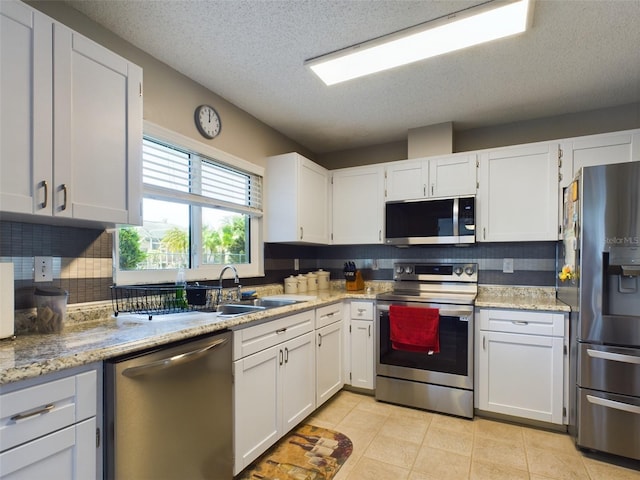 kitchen with light tile patterned floors, decorative backsplash, appliances with stainless steel finishes, white cabinetry, and a textured ceiling