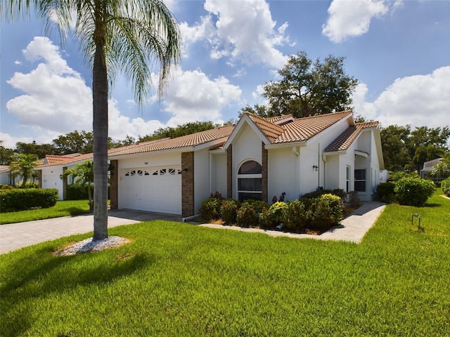 mediterranean / spanish house with stucco siding, an attached garage, a front yard, driveway, and a tiled roof