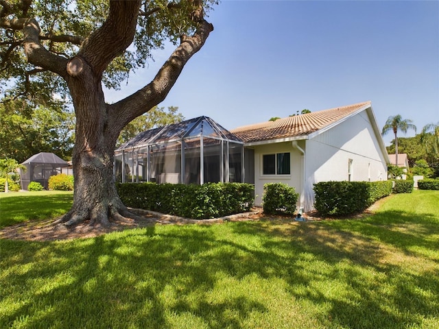 back of house featuring a yard, a tile roof, a lanai, and stucco siding