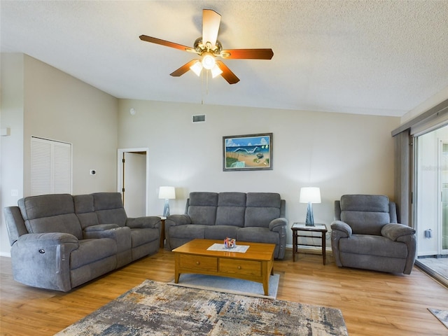 living room featuring lofted ceiling, light wood finished floors, a textured ceiling, and visible vents