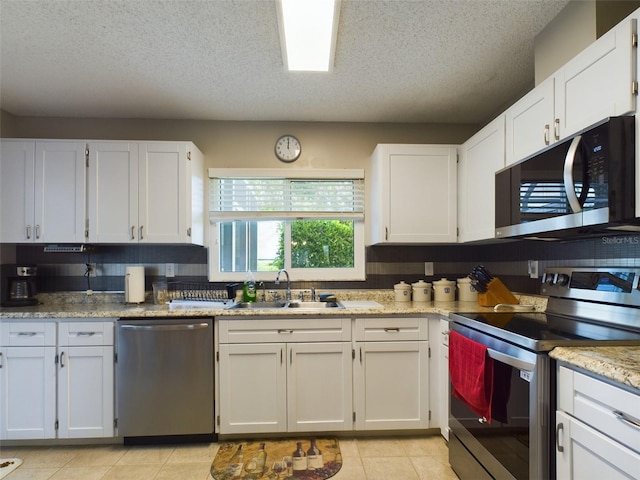 kitchen with light tile patterned floors, white cabinets, stainless steel appliances, a textured ceiling, and a sink