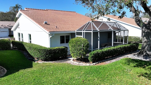 rear view of property featuring a lanai, a tile roof, a yard, and stucco siding