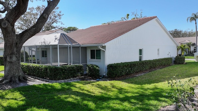 back of property featuring a lanai, a tile roof, a yard, and stucco siding