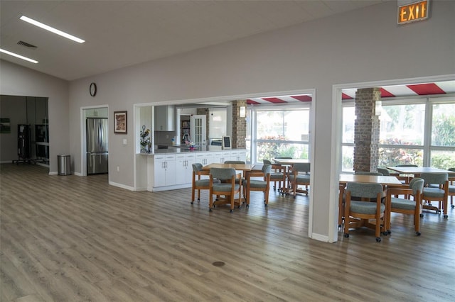 dining room featuring a healthy amount of sunlight, visible vents, vaulted ceiling, and wood finished floors