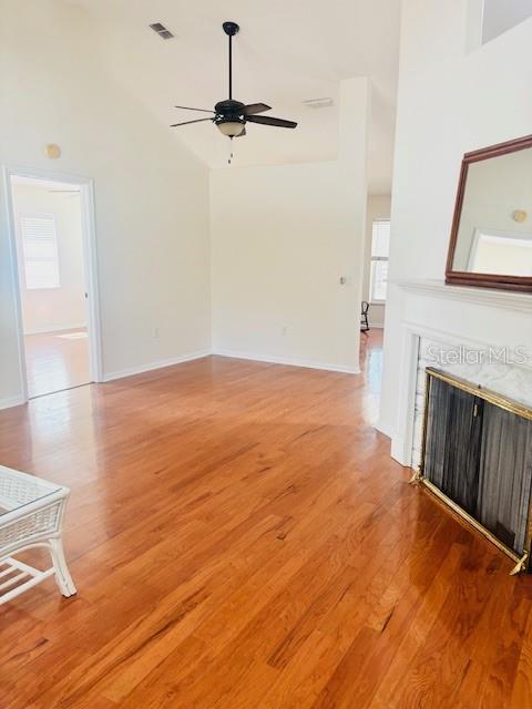 unfurnished living room with light wood finished floors, visible vents, a ceiling fan, a premium fireplace, and high vaulted ceiling