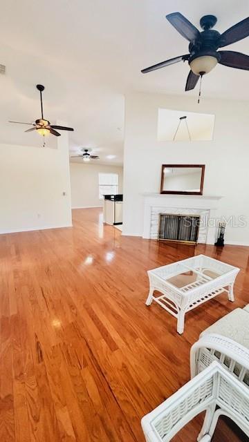 unfurnished living room with ceiling fan, visible vents, a fireplace, and wood finished floors