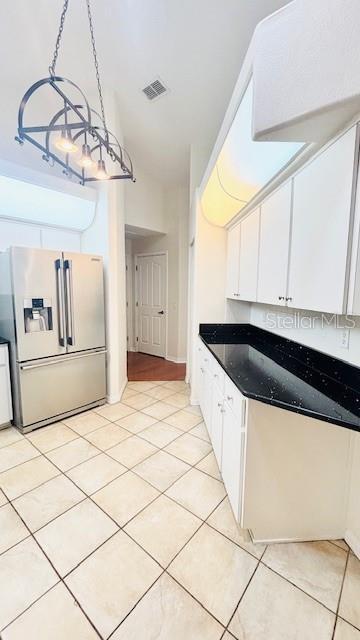 kitchen with stainless steel refrigerator with ice dispenser, light tile patterned floors, dark countertops, visible vents, and white cabinetry