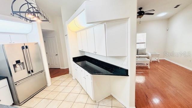 kitchen featuring refrigerator with ice dispenser, dark countertops, ceiling fan, light wood-style flooring, and white cabinetry