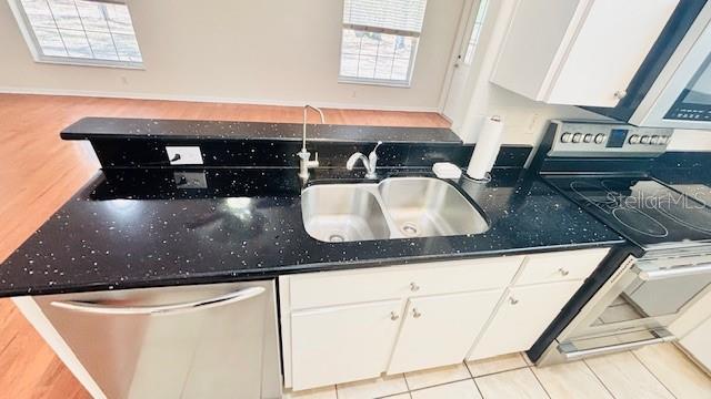 kitchen with appliances with stainless steel finishes, white cabinetry, a sink, and light tile patterned flooring