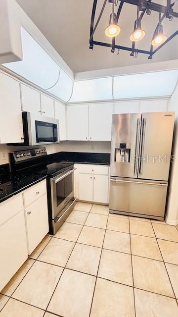 kitchen featuring dark countertops, light tile patterned floors, appliances with stainless steel finishes, and white cabinets