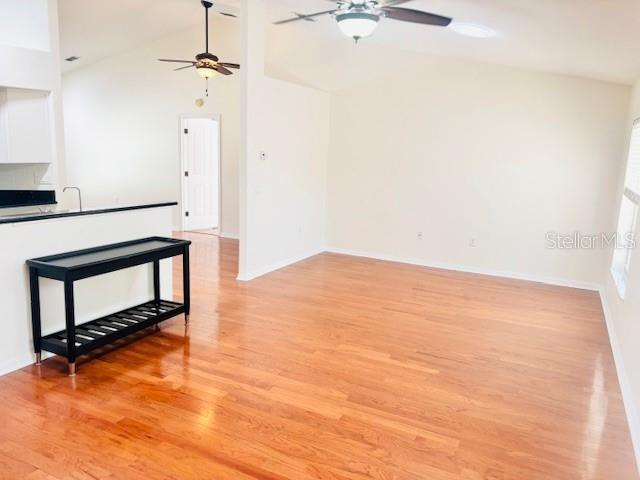 empty room with ceiling fan, high vaulted ceiling, light wood-type flooring, and baseboards