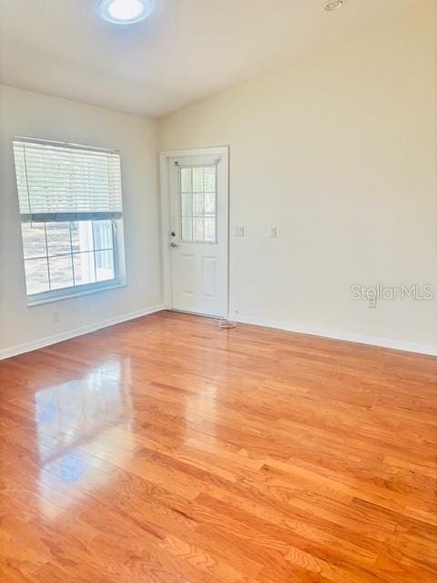 unfurnished room with light wood-type flooring, lofted ceiling, and baseboards