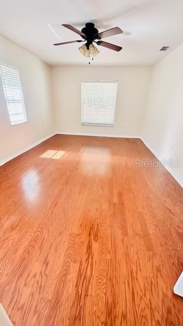 empty room featuring ceiling fan, wood finished floors, visible vents, and baseboards