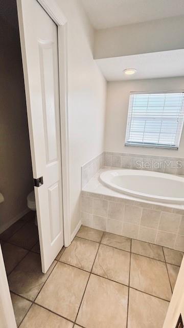 bathroom featuring toilet, tile patterned flooring, baseboards, and a bath