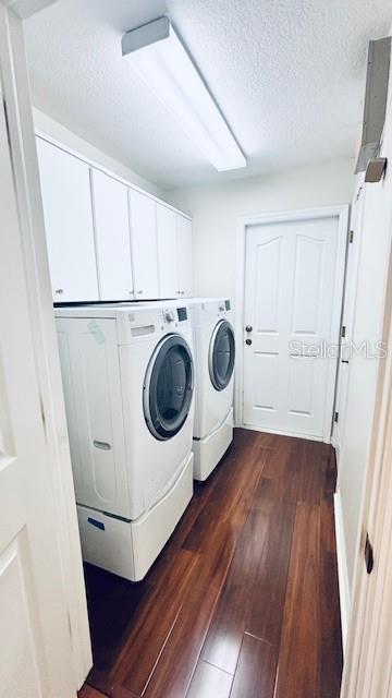 laundry area with cabinet space, a textured ceiling, washer and clothes dryer, and dark wood-type flooring