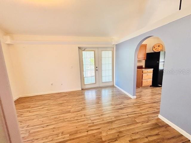 spare room with light wood-type flooring, baseboards, arched walkways, and french doors