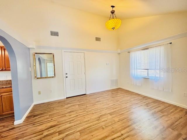 spare room with visible vents, arched walkways, light wood-style flooring, and baseboards