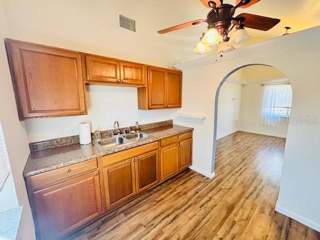 kitchen featuring arched walkways, visible vents, light wood-style flooring, brown cabinetry, and a sink