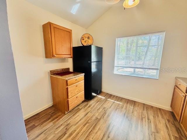 kitchen with baseboards, vaulted ceiling, light wood-type flooring, freestanding refrigerator, and brown cabinets