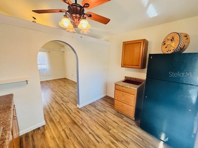 kitchen featuring arched walkways, brown cabinetry, baseboards, light wood-style flooring, and freestanding refrigerator