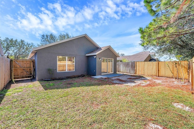 rear view of property featuring a yard, a fenced backyard, a gate, and stucco siding