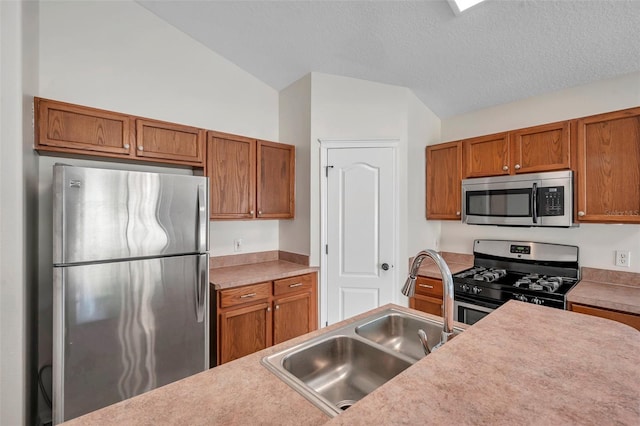 kitchen with light countertops, appliances with stainless steel finishes, brown cabinetry, vaulted ceiling, and a sink