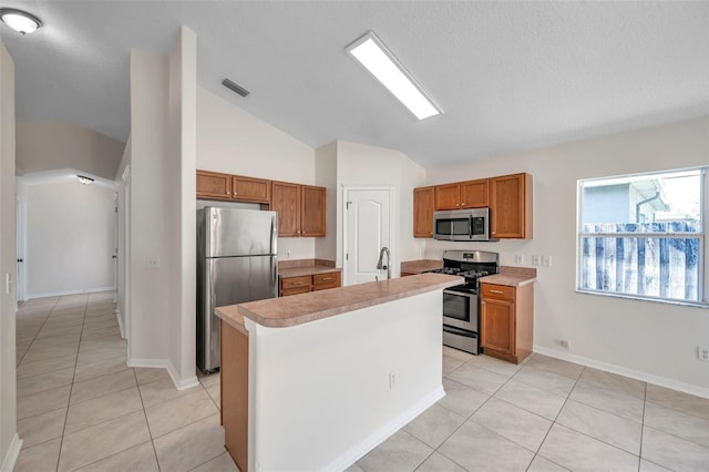 kitchen with lofted ceiling, a kitchen island with sink, light countertops, appliances with stainless steel finishes, and brown cabinetry