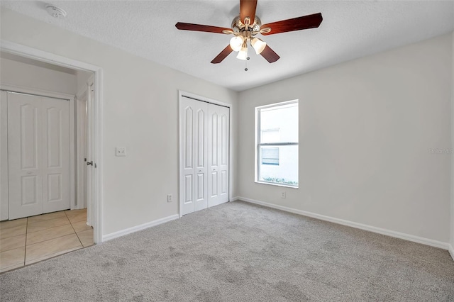 unfurnished bedroom with light tile patterned floors, a closet, light colored carpet, a textured ceiling, and baseboards