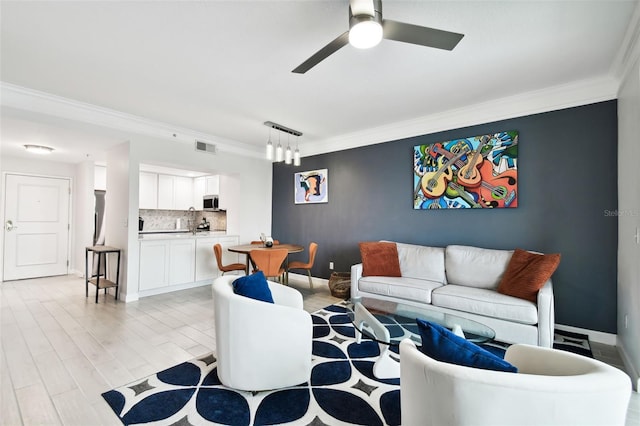 living room with visible vents, light wood-style floors, crown molding, baseboards, and ceiling fan