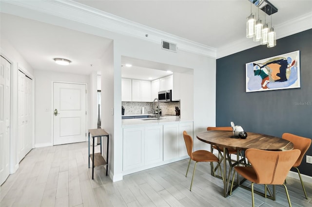 dining room featuring visible vents, light wood-type flooring, baseboards, and ornamental molding