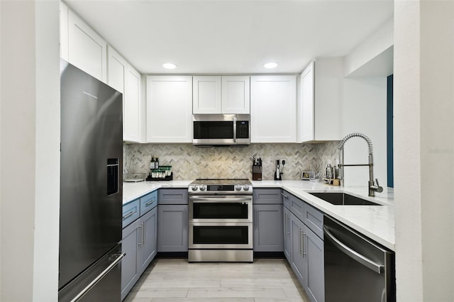 kitchen with backsplash, gray cabinetry, appliances with stainless steel finishes, white cabinets, and a sink