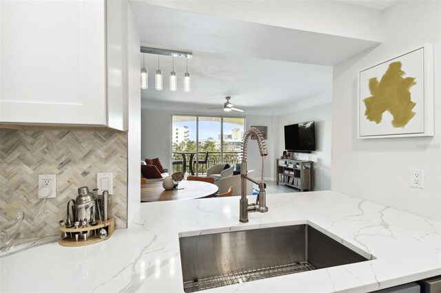 kitchen featuring light stone counters, a sink, decorative backsplash, white cabinets, and open floor plan