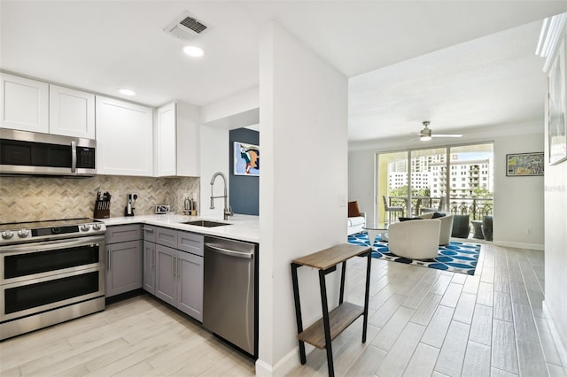 kitchen with visible vents, gray cabinetry, light wood-style flooring, stainless steel appliances, and decorative backsplash